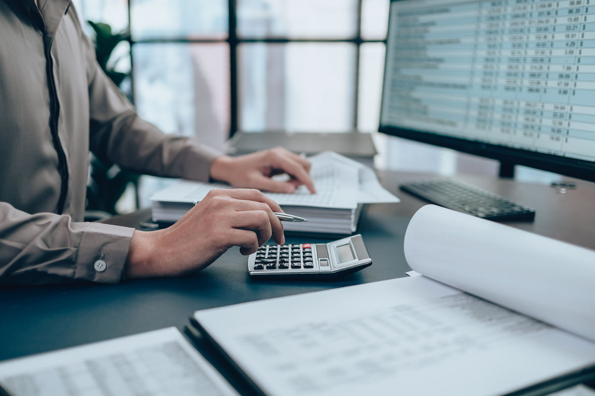 A man with a calculator inputting data into a spreadsheet on a computer