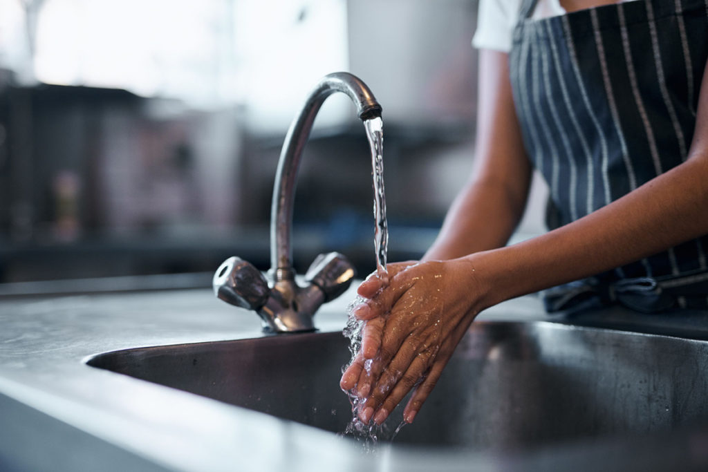 Person in an apron washing their hands with water over a sink