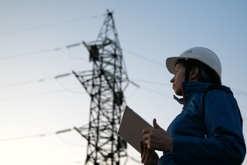 Someone completing an energy audit in front of an electricity pylon