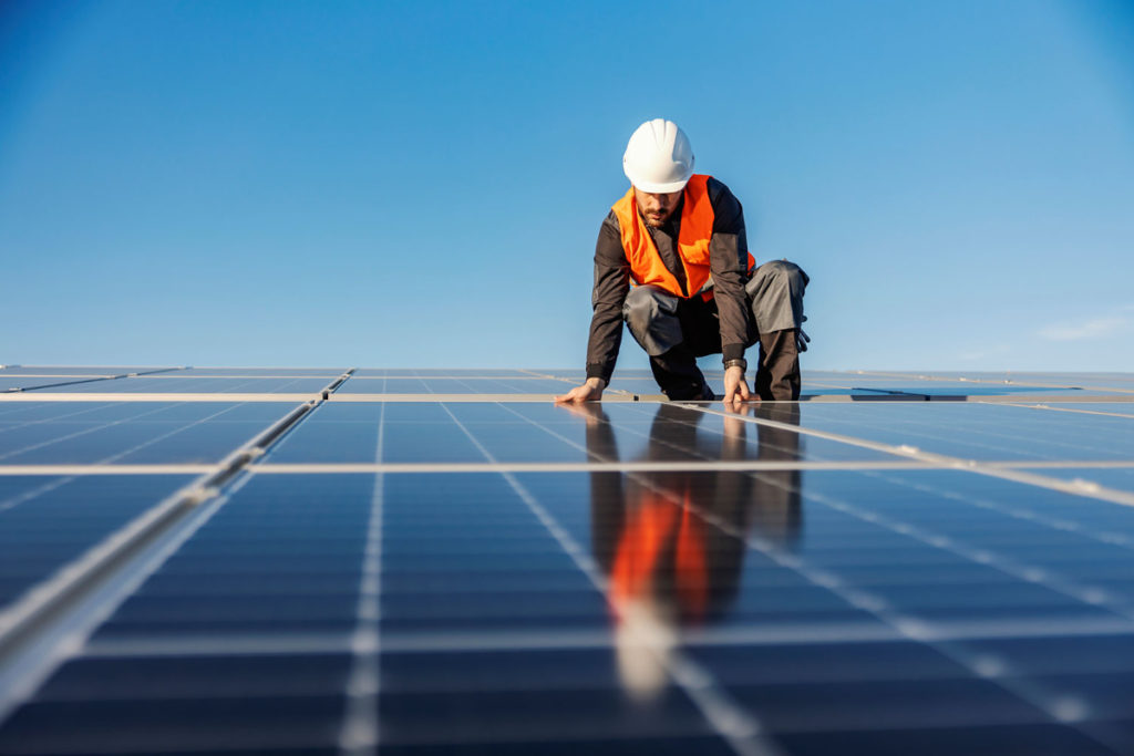 A man in a high vis jacket installing solar panels for an export meter on a roof