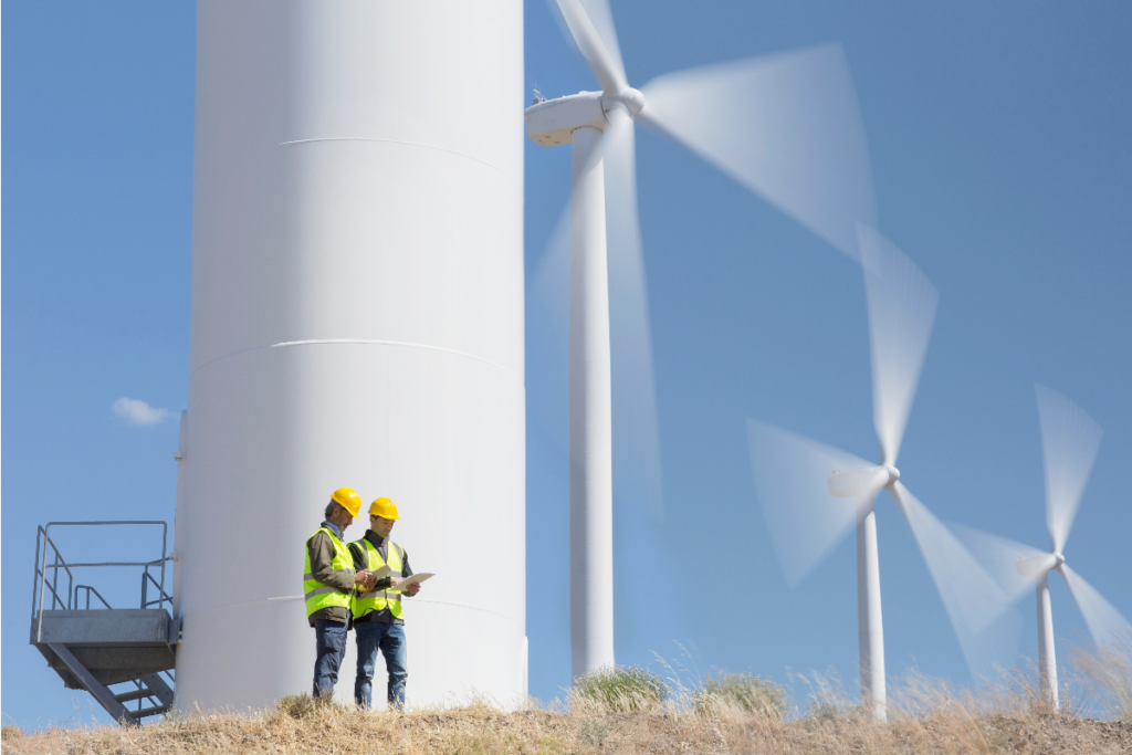 Two people in hi-vis working on a site with wind turbines in the background